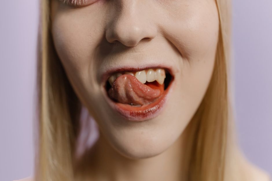 Close-up portrait of a blonde woman with her tongue out against a neutral background.